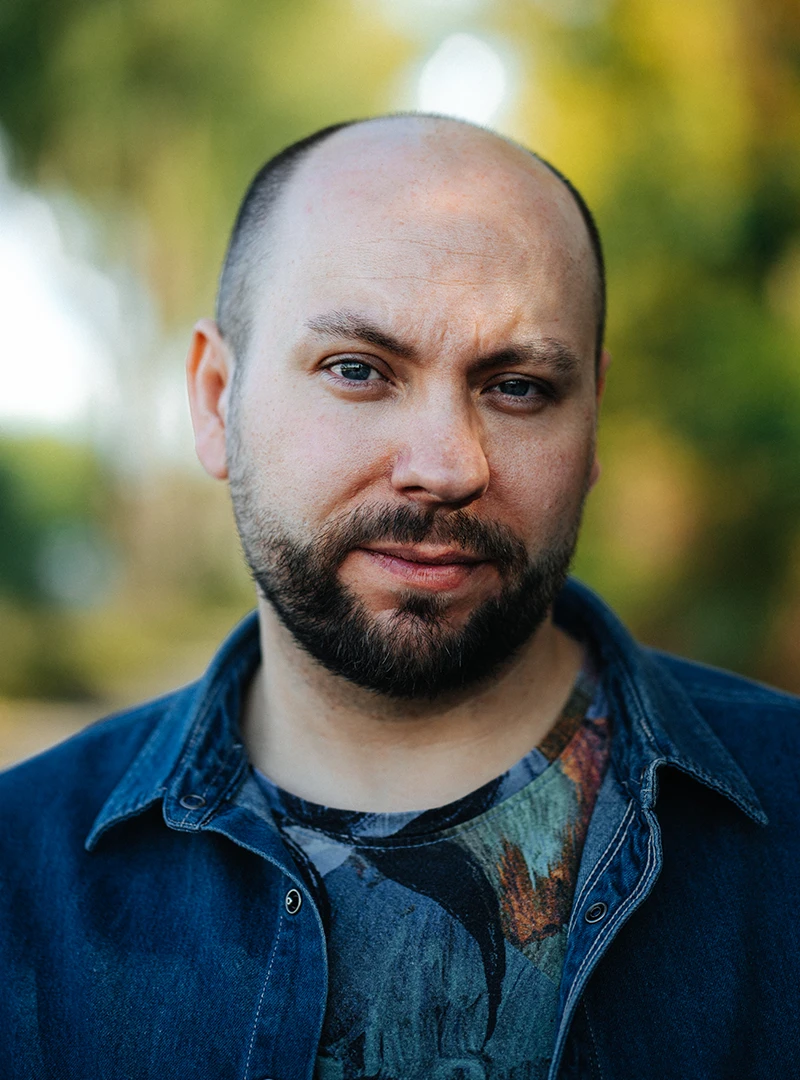 Der Regisseur & Autor Lars Smekal steht vor einem grünen Hintergrund, er trägt ein blaues Hemd.